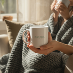 Close up of PAUSE sage green mug held in hands in a cosy home setting